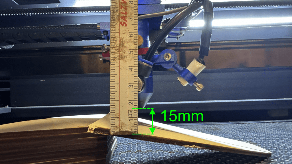 Laserkopf über der schmalsten Stelle der Gravurlinie. Fokus am Laser ermitteln mit einem Zollstock. Dieser wird angehalten und zeigt den Fokusabstand von 15mm.